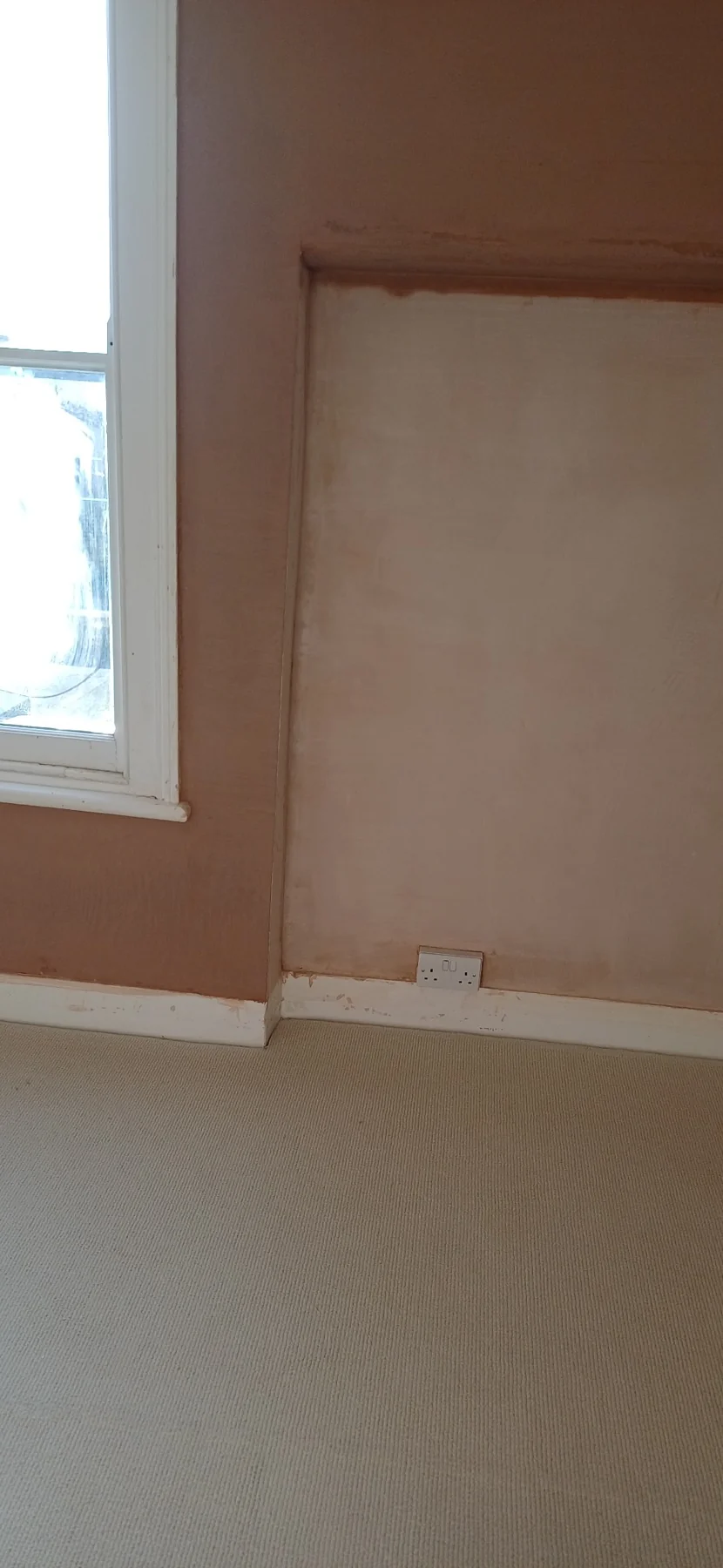 Skimmed alcove wall beside a window, with a socket above the skirting, in Brentford.