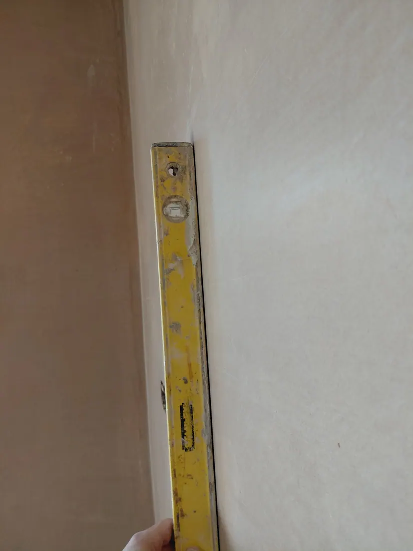 Spirit level held against a newly plastered interior wall
