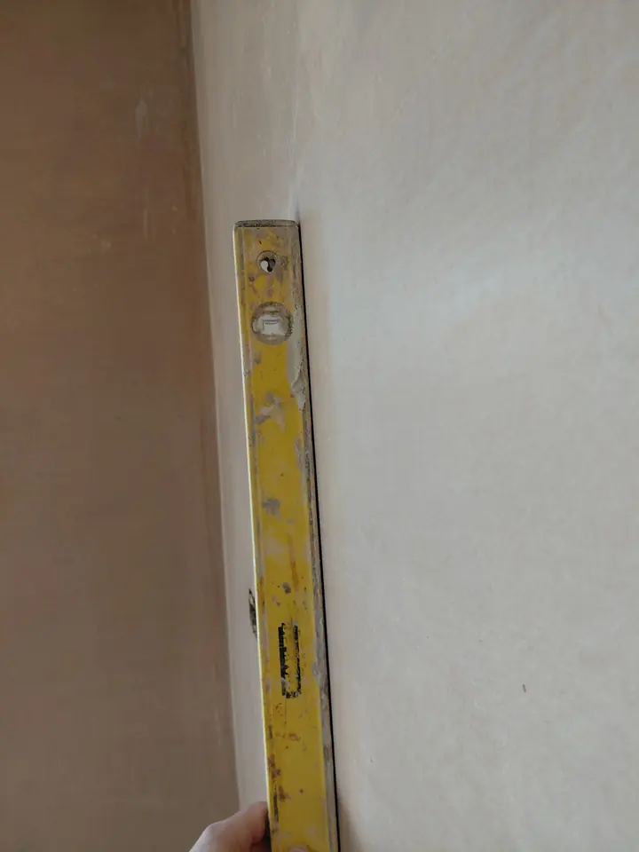 Our plasterer holding a long spirit level against an interior wall to check its straightness