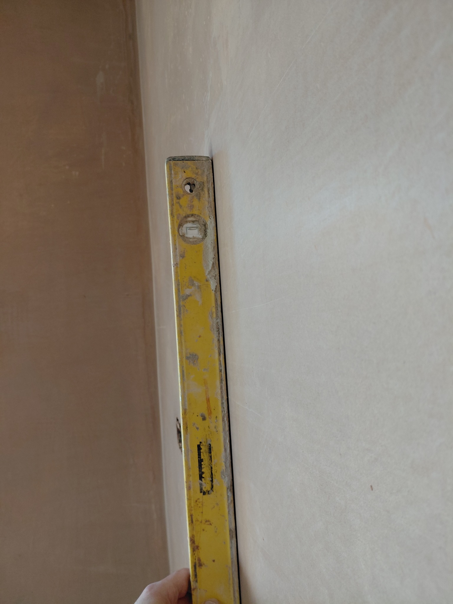 Spirit level held against a newly plastered interior wall